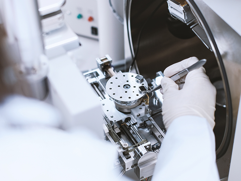 A close up photograph of a researcher's hand placing a sample with a tweezer to a the scientific device.