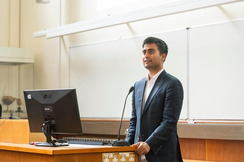 Dr Navoneel Sen standing by a lecturn, smiling, as he gives a lecture during the 5th birthday symposium held by Oxford's Kavli Institute for Nanoscience Discovery (Kavli INsD)