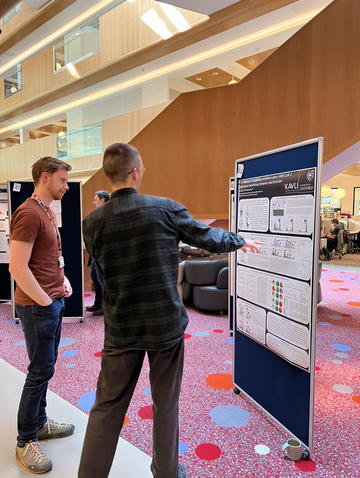 A photograph of Sean Burnap presenting his poster to a colleague. 