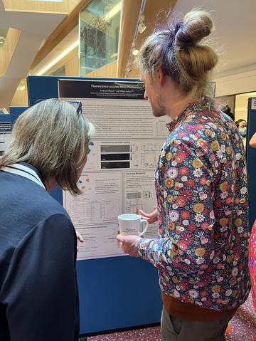 A photograph of Emanuel Pfitzner presenting his poster to a colleague.