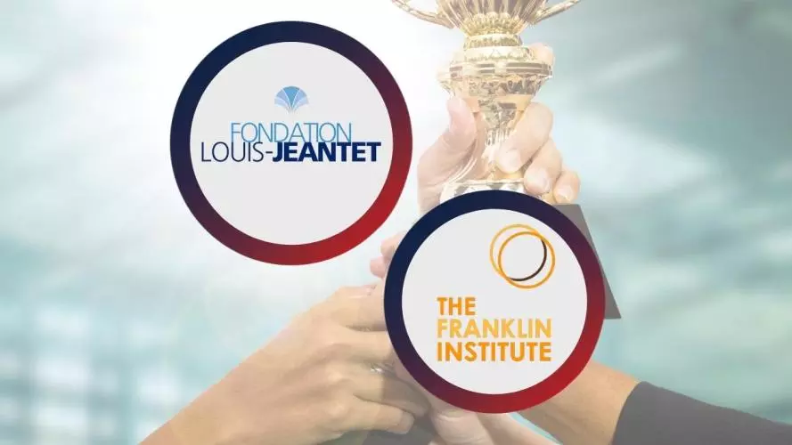 An image with "Louis-Jeantet Foundation logo" and "Benjamin Franklin Institute logo" in front of a background with hands holding a golden award.