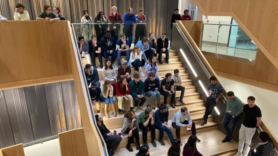 Kavli Oxford researchers listening to presentations while standing and sitting on the main stairway