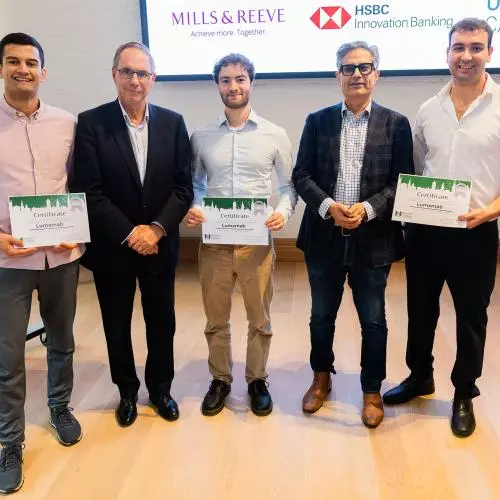 Five men pose together indoors, with three holding certificates. A screen behind them displays Mills & Reeve, HSBC Innovation Banking, and Oxford Capital logos.